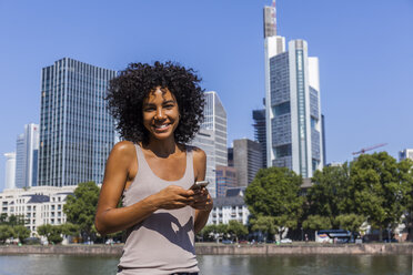 Germany, Frankfurt, portrait of smiling young woman with smartphone in the city - TCF05570