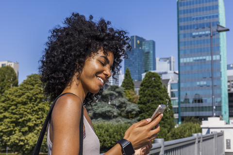 Deutschland, Frankfurt, lächelnde junge Frau mit lockigem Haar, die auf ihr Mobiltelefon schaut, lizenzfreies Stockfoto