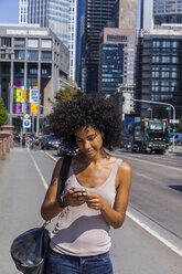Germany, Frankfurt, smiling young woman with curly hair using cell phone - TCF05575