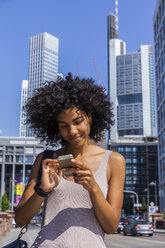 Deutschland, Frankfurt, Porträt einer lächelnden jungen Frau mit lockigem Haar, die ein Mobiltelefon benutzt - TCF05576