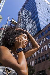 Germany, Frankfurt, portrait of young woman with smartwatch on the phone in front of skyscrapers - TCF05581