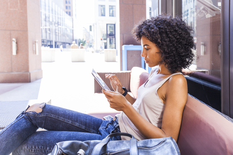 Junge Frau sitzt in einem Straßencafé und benutzt ein digitales Tablet, lizenzfreies Stockfoto