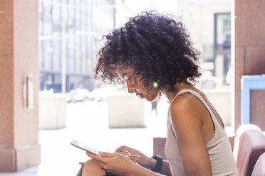 Junge Frau mit lockigem Haar sitzt in einem Straßencafé und benutzt ein digitales Tablet - TCF05591