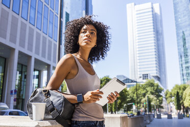 Deutschland, Frankfurt, Portrait einer jungen Frau mit Reisetasche, Tablet und Coffee to go in der Stadt - TCF05599