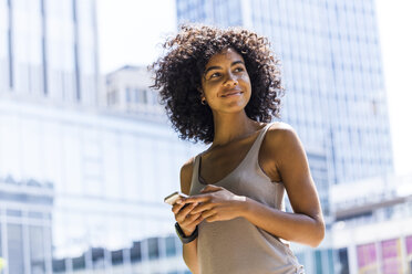 Germany, Frankfurt, portrait of smiling young woman with curly hair in front of skyscrapers - TCF05613