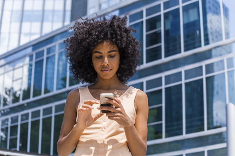 Deutschland, Frankfurt, Porträt einer jungen Frau mit lockigem Haar, die ein Smartphone benutzt, lizenzfreies Stockfoto