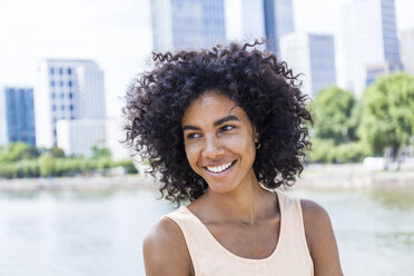 Germany, Frankfurt, portrait of smiling young woman with curly hair in front of Main River - TCF05628