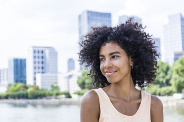 Germany, Frankfurt, portrait of smiling young woman with curly hair in front of Main River - TCF05629