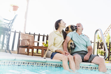 A couple sitting on the edge of a swimming pool, with their dogs. - MINF07159