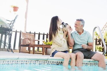 A couple sitting on the edge of a swimming pool, with their dog. - MINF07161