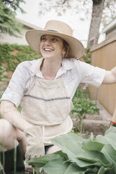 A woman in a wide brimmed straw hat working in a garden, digging. - MINF07164