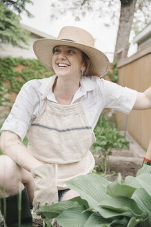 Eine Frau mit einem breitkrempigen Strohhut arbeitet in einem Garten und gräbt. - MINF07164