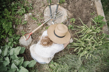 Eine Frau mit einem breitkrempigen Strohhut arbeitet in einem Garten und gräbt. - MINF07165
