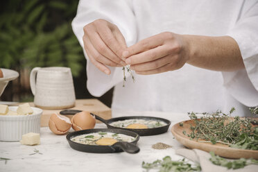 A woman adding herbs to the eggs cracked into two small pans. - MINF07179