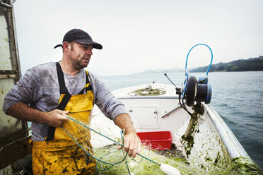 A fisherman on a boat hauling in the fishing net. - MINF07190