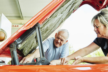 Ältere Frau und älterer Mann reparieren ein Auto und schauen unter die Motorhaube. - MINF07212