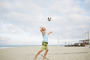 Mature man standing on a beach, playing beach volleyball. - MINF07216