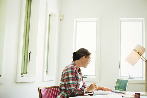 Eine Frau sitzt zu Hause am Schreibtisch und arbeitet. - MINF07235