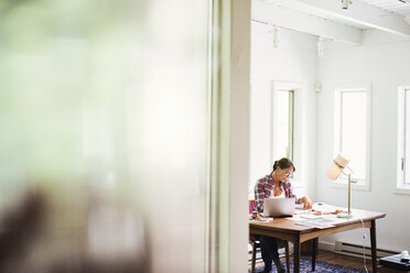 Eine Frau arbeitet am Schreibtisch in einem Arbeitszimmer zu Hause. - MINF07242