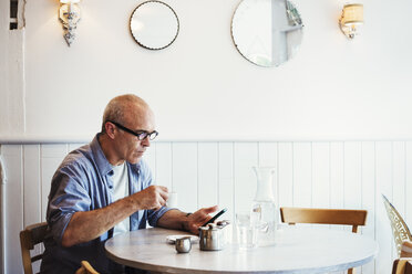 Ein Mann, der an einem Tisch sitzt und sein Smartphone überprüft. - MINF07251