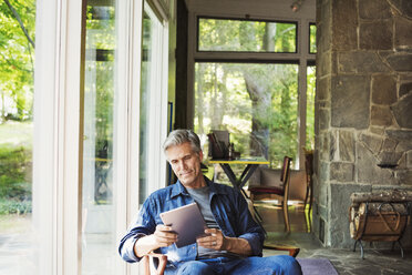 Ein Mann sitzt an einem Fenster und liest mit einem digitalen Tablet. - MINF07261