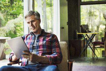 A man seated by a window reading using a digital tablet. - MINF07262