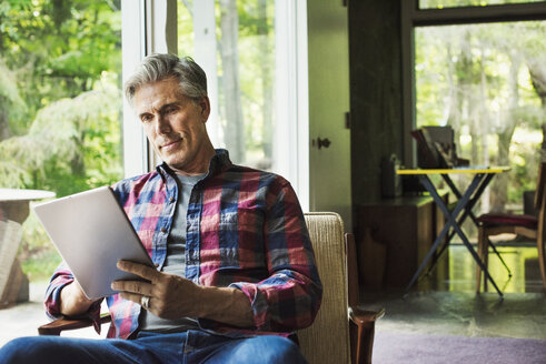 Ein Mann sitzt an einem Fenster und liest mit einem digitalen Tablet. - MINF07262