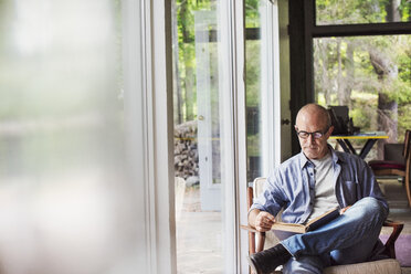 A man seated by a window reading a book. Blurred foreground. - MINF07264