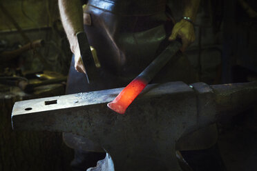 Ein Schmied schlägt in einer Werkstatt mit einem Hammer ein Stück glühendes Metall auf einen Amboss. - MINF07283