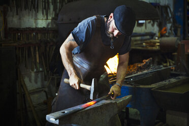 A blacksmith strikes a length of red hot metal on an anvil with a hammer in a workshop. - MINF07287