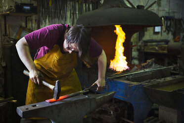 Ein Schmied schlägt in einer Werkstatt mit einem Hammer ein Stück glühendes Metall auf einen Amboss. - MINF07291