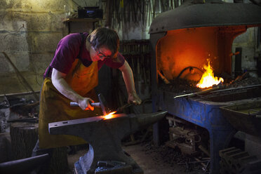A blacksmith striking red hot metal on an anvil inside a workshop. - MINF07297