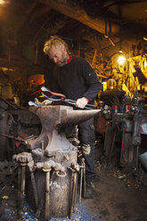 Blacksmith standing at an anvil in his workshop. - MINF07299