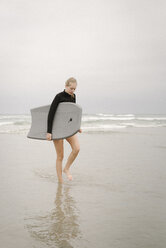 Blondes Mädchen, das an einem Sandstrand entlangläuft und ein Bodyboard trägt. - MINF07329