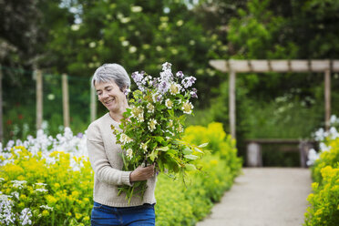 A florist selecting flowers and plants from the garden to create an arrangement. Organic garden. - MINF07345