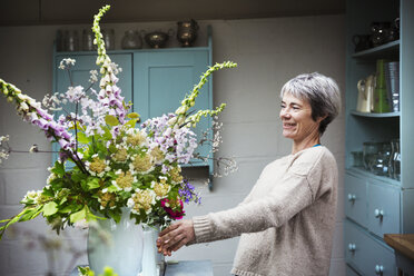 A florist working on a tall vase arrangement of flowers. - MINF07346