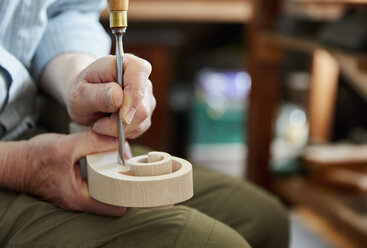 A violin maker using hand tools to smooth and finish a new wooden violin headstock, curled scroll of wood. - MINF07381