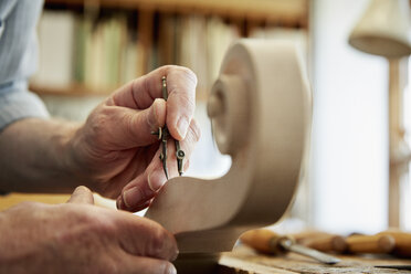 Ein Geigenbauer bei der Arbeit in seiner Werkstatt, der mit Handwerkzeugen die gewellte Schnecke des Geigenstocks formt und ziseliert. - MINF07382