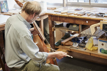 A violin maker in his workshop playing an instrument with a bow, tuning and finishing. - MINF07389