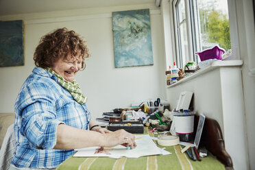 Eine Künstlerin arbeitet an einem Tisch, benutzt einen großen blauen Pastellstift und zeichnet auf Papier. - MINF07409