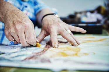Ein Künstler bei der Arbeit, die Hände zeichnen mit gelber Pastellfarbe auf die Oberfläche einer Leinwand. - MINF07410
