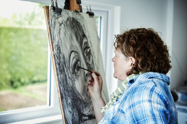 An artist working at her easel, using charcoal on paper drawing a portrait. - MINF07412