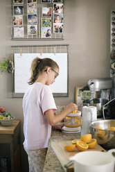 Eine Familie bereitet das Frühstück in einer Küche vor, ein Mädchen presst Orangen aus. - MINF07414