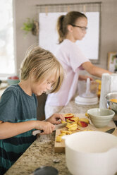 Family preparing breakfast in a kitchen, boy cutting fruit. - MINF07417