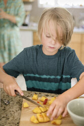 Family preparing breakfast in a kitchen, boy cutting fruit. - MINF07418