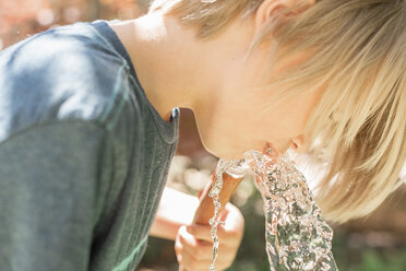 Boy standing in a garden, drinking water from a garden hose. - MINF07423