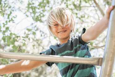 Blonder Junge auf einem Klettergerüst in einem Garten. - MINF07425