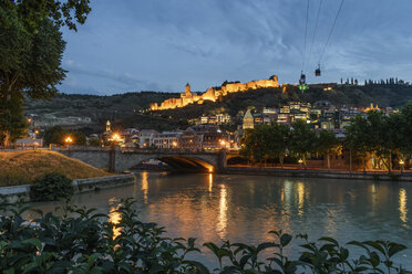 Brücke über den Fluss Kura und beleuchtete Festung auf einem Hügel, Tiflis, Georgien, bei Sonnenuntergang. - MINF07480
