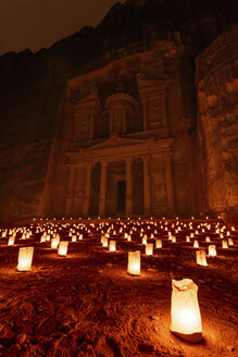 Außenansicht der Felsenhöhlen und der Architektur der Sandsteinfassade von Al Khazneh oder der Schatzkammer in Petra, Jordanien, bei Nacht. Ein roter Schein mit kleinen glühenden Lampen auf dem Boden. - MINF07495