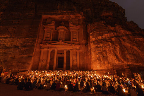 Außenansicht der in Fels gehauenen Architektur von Al Khazneh oder der Schatzkammer in Petra, Jordanien, mit einer großen Gruppe von Menschen, die nachts auf dem Boden sitzen. - MINF07496